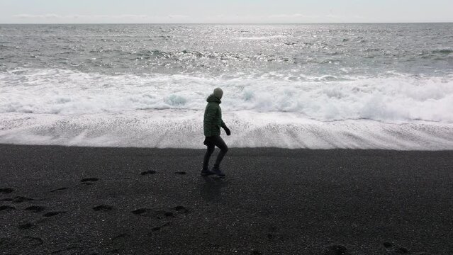 Man running from tide on black sand beach