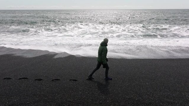 Man walking along black sand beach with sea
