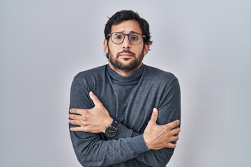 Handsome latin man standing over isolated background shaking and freezing for winter cold with sad...
