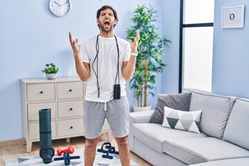 Handsome latin man wearing sportswear at home crazy and mad shouting and yelling with aggressive expression and arms raised. frustration concept.