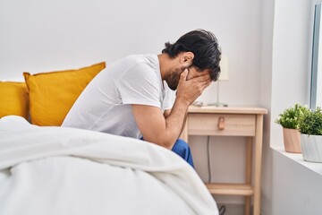 Young hispanic man sitting on bed crying at bedroom