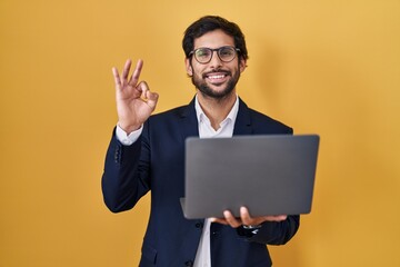 Handsome latin man working using computer laptop smiling positive doing ok sign with hand and fingers. successful expression.