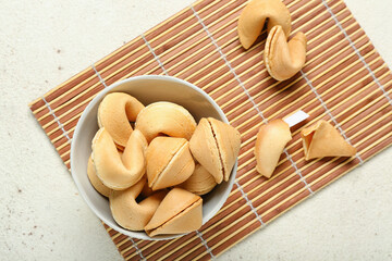 Bamboo mat with bowl of fortune cookies on light background
