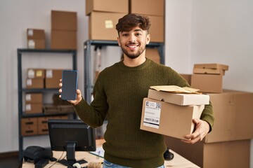 Arab man with beard working at small business ecommerce holding delivery packages smiling with a...