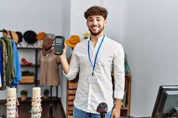 Young arab man smiling confident holding data phone device at clothing store