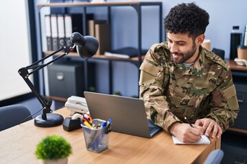 Young arab man army soldier using laptop writing on notebook at office