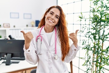 Young redhead woman wearing doctor uniform and stethoscope at the clinic success sign doing positive gesture with hand, thumbs up smiling and happy. cheerful expression and winner gesture.