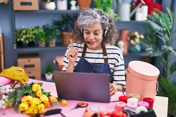 Middle age woman with grey hair working at florist with laptop smiling with an idea or question pointing finger with happy face, number one