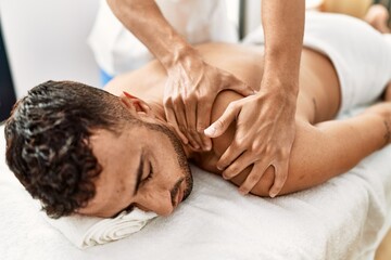 Fototapeta na wymiar Two hispanic men physiotherapist and patient having rehab session massaging back at beauty center