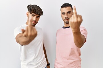 Young gay couple standing over isolated background showing middle finger, impolite and rude fuck...