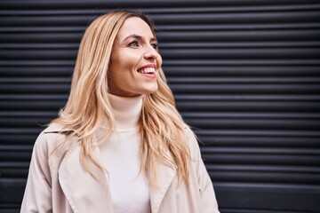 Young blonde woman smiling confident looking to the side over isolated black metal background