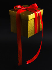 Hanging in the air golden kraft paper gift box with red ribbon on black background