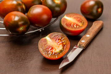 Knife and two halves of a tomato. Whole tomatoes on a metal stand.
