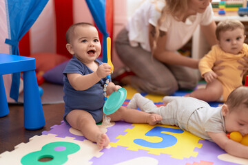 Group of toddlers playing with dish toy sitting on floor at kindergarten