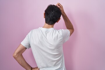 Young hispanic man standing over pink background backwards thinking about doubt with hand on head