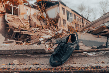 A dark blue shoe lies against the background of a destroyed house. War in Ukraine