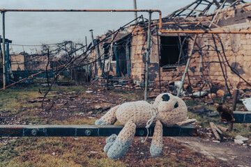 Countryside. Toy (teddy bear) against the background of a house destroyed by shelling