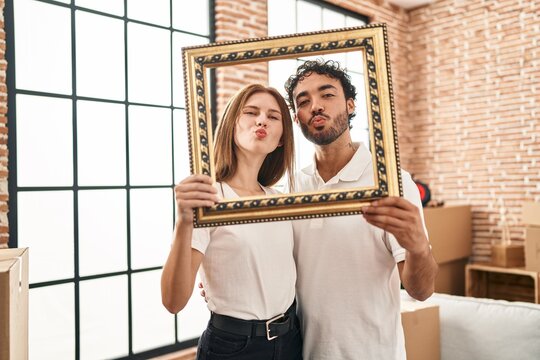 Young two people holding empty frame together looking at the camera blowing a kiss being lovely and sexy. love expression.