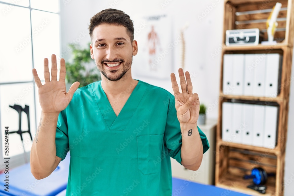 Wall mural young physiotherapist man working at pain recovery clinic showing and pointing up with fingers numbe