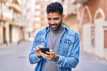 Young hispanic man smiling confident using smartphone at street