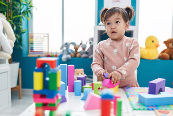 Adorable chinese girl playing with construction blocks standing at kindergarten