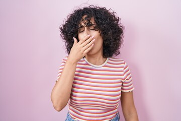 Young middle east woman standing over pink background bored yawning tired covering mouth with hand. restless and sleepiness.
