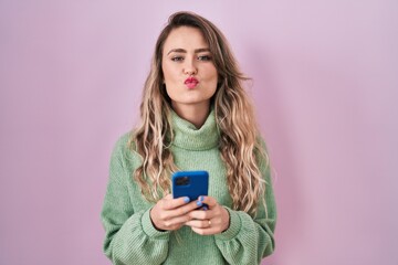 Young caucasian woman using smartphone typing message looking at the camera blowing a kiss being lovely and sexy. love expression.