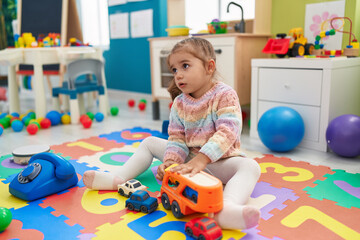 Adorable hispanic girl playing with car toy sitting on floor at kindergarten