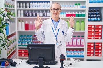 Young caucasian woman working at pharmacy drugstore showing and pointing up with fingers number nine while smiling confident and happy.