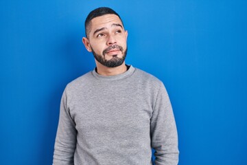 Fototapeta premium Hispanic man standing over blue background smiling looking to the side and staring away thinking.
