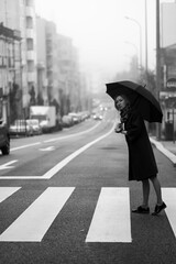 A woman with an umbrella stands by the road in cloudy weather. Black and white photo.