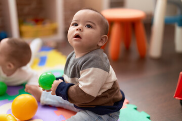 Adorable chinese toddler playing with ball sitting on floor at kindergarten