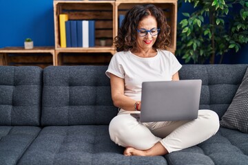 Middle age hispanic woman using laptop sitting on the sofa at home