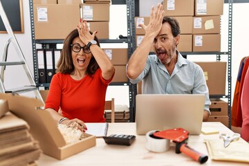 Middle age couple working at small business ecommerce surprised with hand on head for mistake,...
