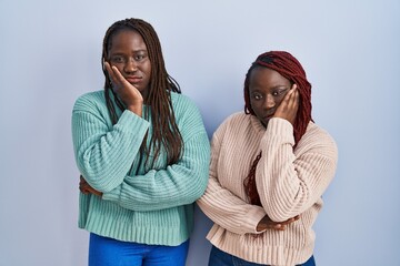 Two african woman standing over blue background thinking looking tired and bored with depression problems with crossed arms.