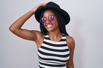 Young african american with braids wearing hat and sunglasses smiling confident touching hair with hand up gesture, posing attractive and fashionable