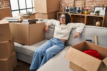 Young hispanic woman smiling confident relaxed sitting o sofa at new home