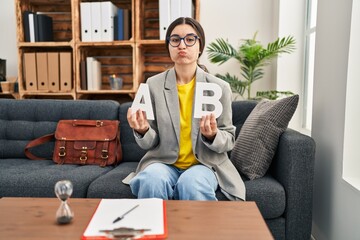 Young hispanic woman working at consultation office puffing cheeks with funny face. mouth inflated...