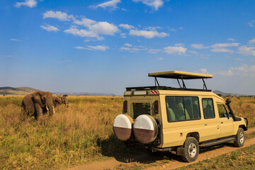 Tourists in SUV car watching and taking photos of african elephants in Serengeti national park, Tanzania. African safari