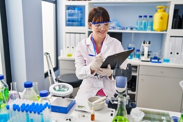 Young beautiful hispanic woman scientist writing report working at pharmacy