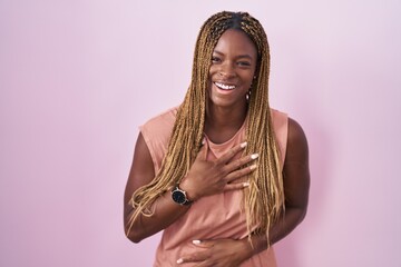 African american woman with braided hair standing over pink background smiling and laughing hard out loud because funny crazy joke with hands on body.