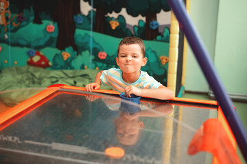 Cheerful little boy plays air hockey and really wants to win. Makes different grimaces