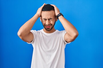 Fototapeta na wymiar Young hispanic man standing over blue background suffering from headache desperate and stressed because pain and migraine. hands on head.