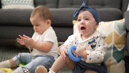 Two toddlers playing with toys crying at home