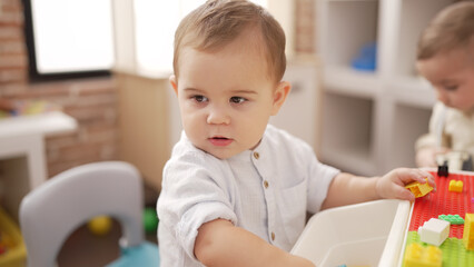 Two adorable toddlers playing with construction blocks sitting on table at kindergarten