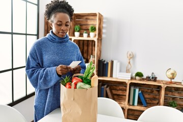 African american woman reading food receipt at home