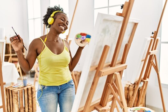 Young african american artist woman using headphones drawing at art studio.