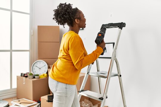 African american woman holding drill standing on ladder at new home