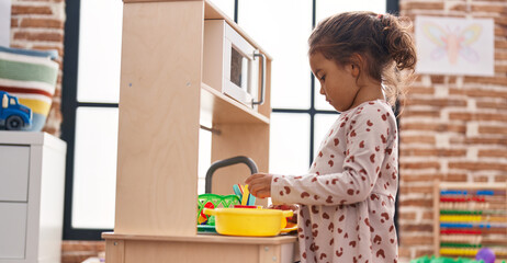 Adorable hispanic girl playing with play kitchen standing at kindergarten