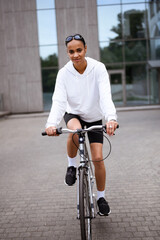 Fototapeta na wymiar Young african american woman in cycling shorts and hoodie looking at camera while biking on street 